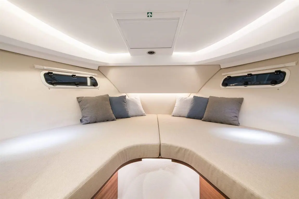 Cozy interior of a yacht cabin featuring cushioned seating, grey pillows, and subtle ambient lighting.